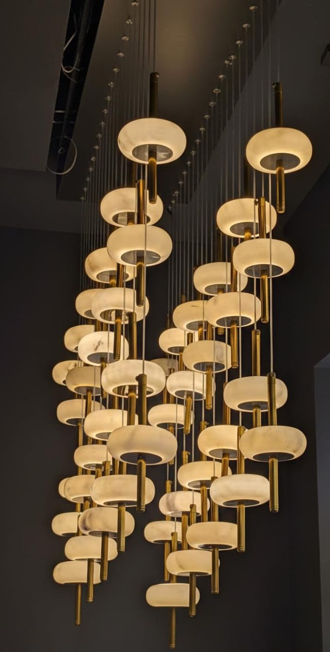 The SpaceAge Chandelier features round frosted glass shades with gold accents, hanging at various heights to form an elegant, artistic cluster of luxury lighting against a dark background.