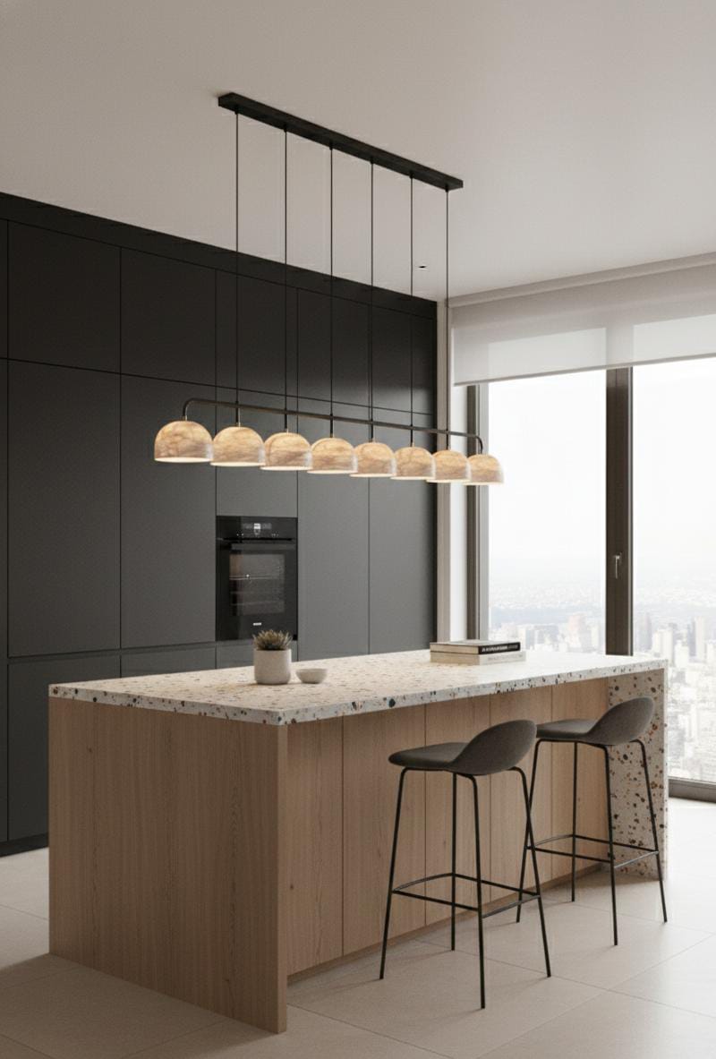 Modern kitchen with matte black cabinets, light wood island, terrazzo countertop, two black bar stools, and modern luxury decor. The Nova Suspension Chandelier highlights the space while a large window frames a city view in the background.